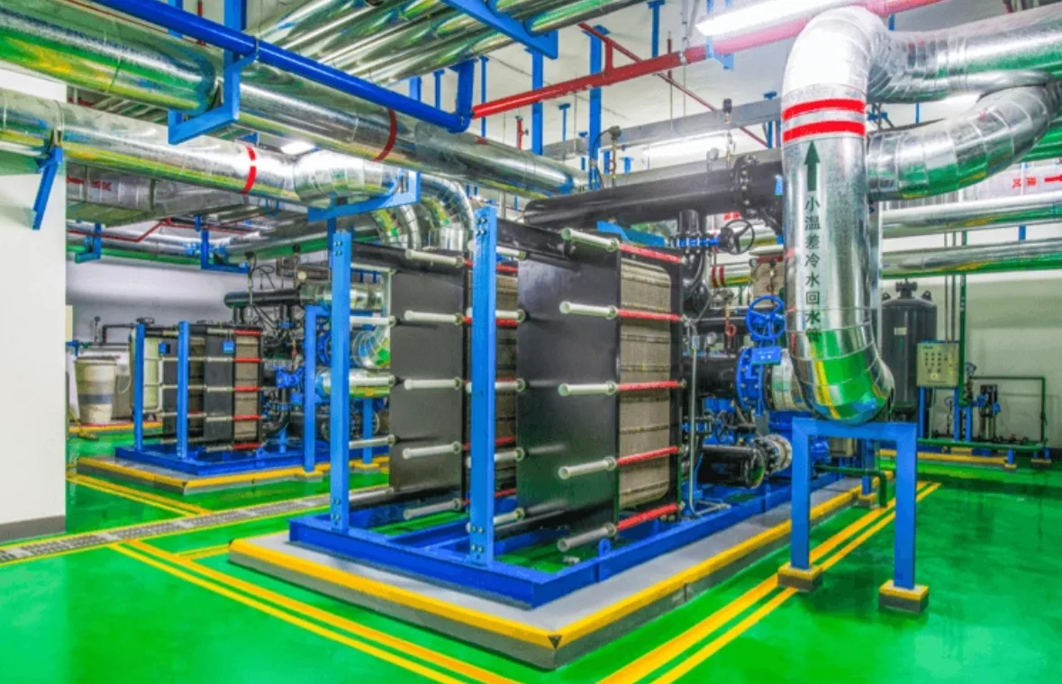 Installed gasketed plate heat exchanger units on blue steel frames in an industrial plant room with insulated chilled water piping